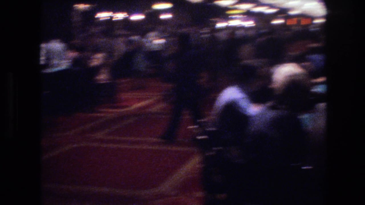 Motion-blurred 8mm pan across Las Vegas casino floor circa 1977, red patterned carpet clearly visible in foreground, patrons rendered indistinct by camera movement.
