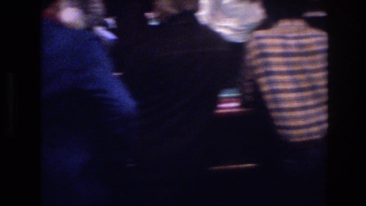 Group of casino patrons seen from behind around a gaming area in a dimly lit casino interior.