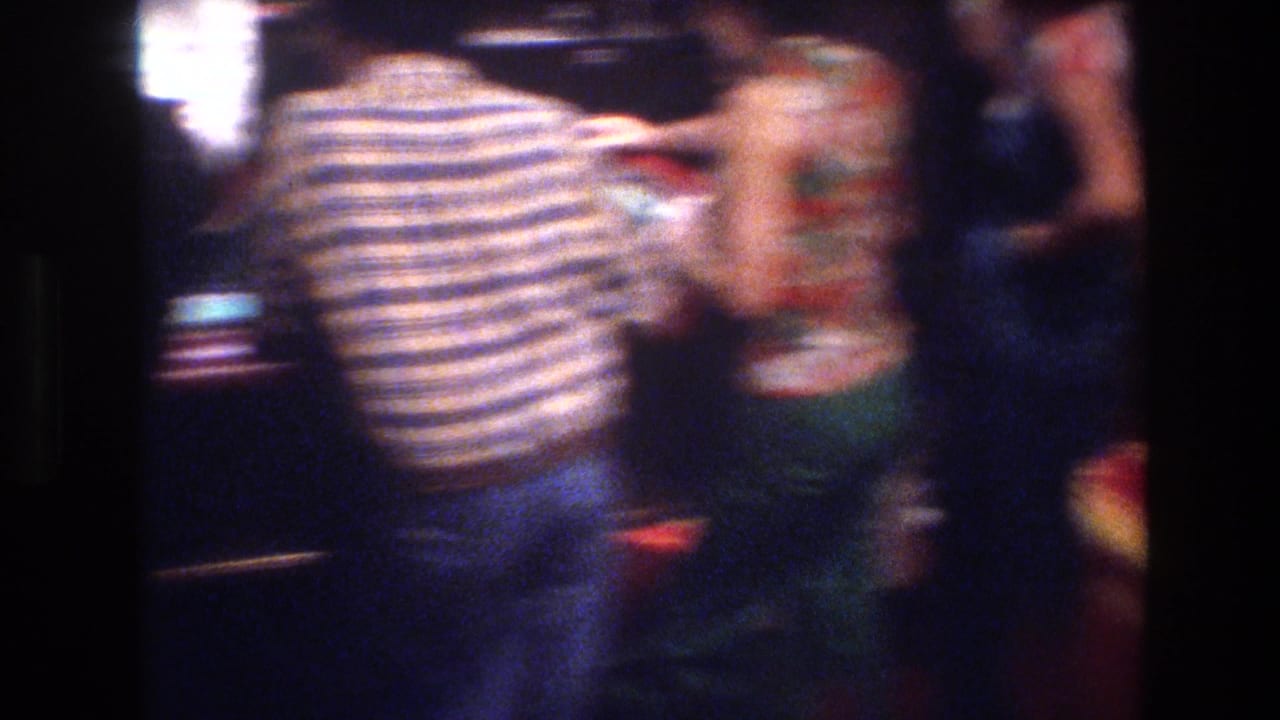 Casino patrons clustered around a gaming area in a Las Vegas casino, circa 1977; man in horizontal-stripe shirt prominent, woman in patterned top partially visible at right.