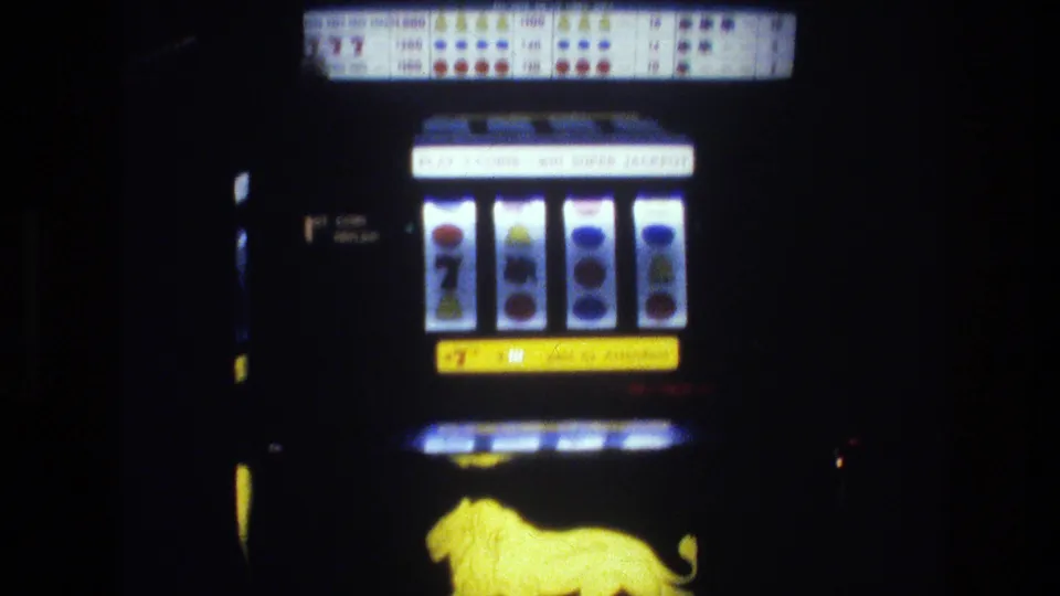 Close-up of a 1970s mechanical slot machine in a Las Vegas casino, circa 1977; illuminated reels showing circle symbols and a 7, printed paytable grid, and yellow animal emblem at base.