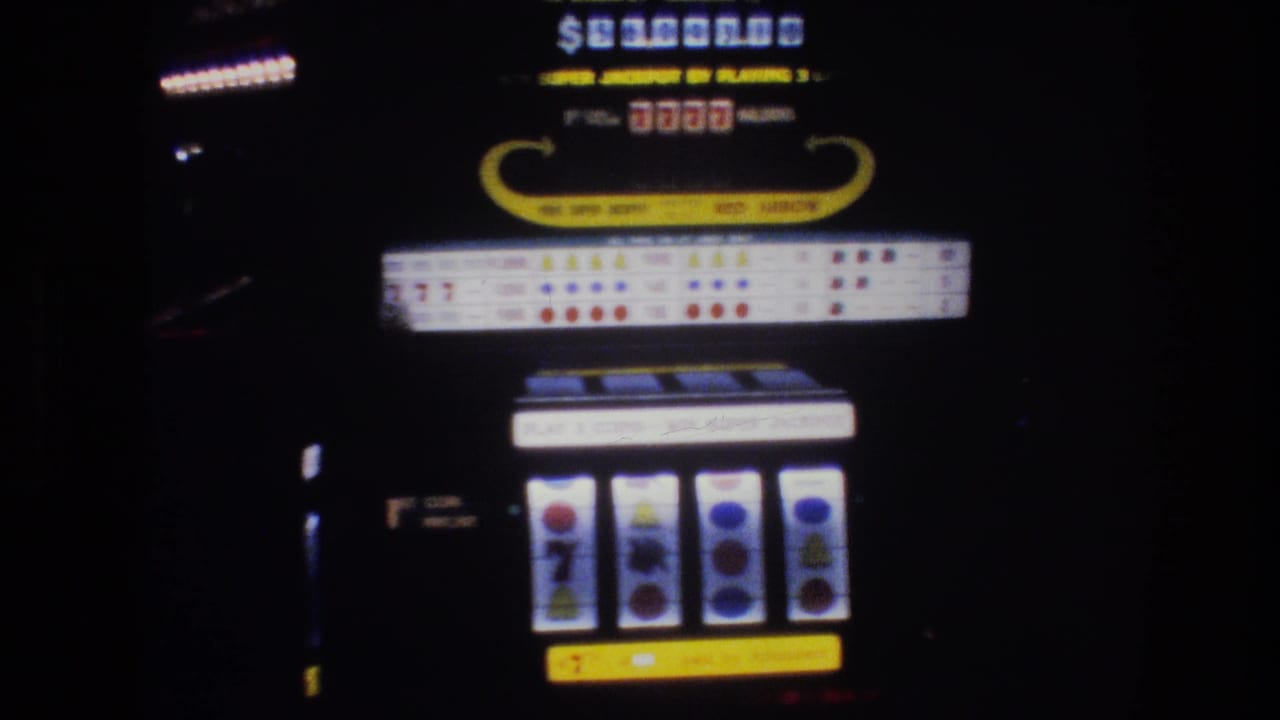 Close-up of a Las Vegas casino slot machine, circa 1977, showing jackpot display, 7777 indicator, and reel symbols in low casino light on 8mm film.
