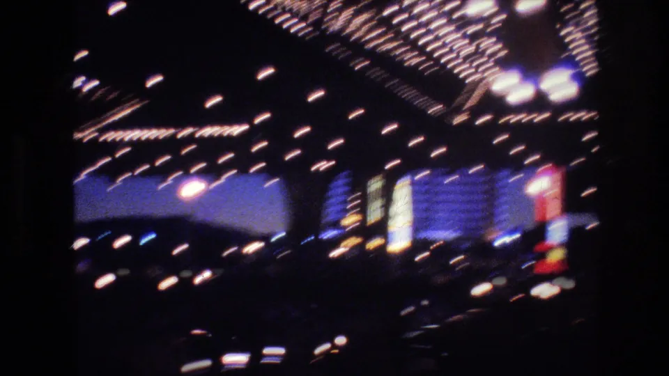 8mm home movie frame of a Las Vegas marquee covered in incandescent holiday bulbs during a handheld camera pan, with neon signs at dusk, circa 1977