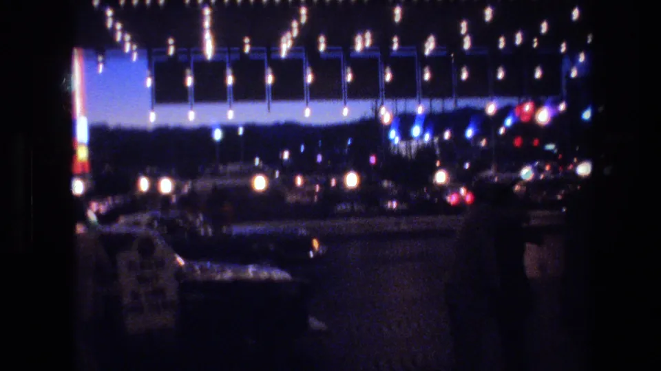 8mm home movie of a Las Vegas hotel or casino exterior decorated with holiday lights at dusk, with street-level vehicles and neon signage visible, circa 1977