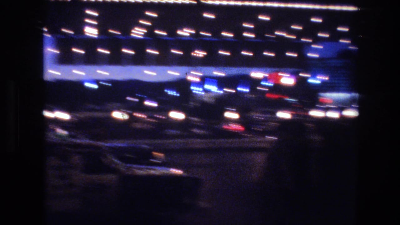 Heavily motion-blurred 8mm frame of white bulb string lights and blue-lit building facade at night