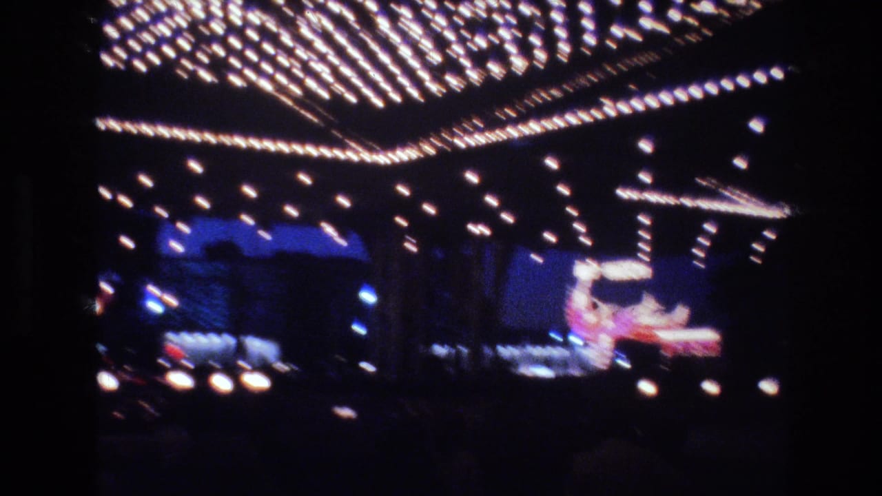 Dense marquee bulb rows above blue-lit commercial facade with colorful holiday display figure at right, Las Vegas area, circa 1977