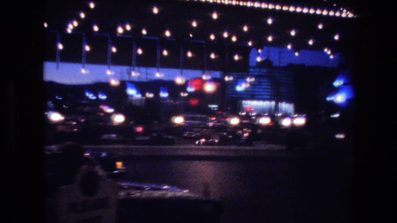 Hanging exposed-bulb strings framing a blue commercial facade with car headlights and red traffic light below, Las Vegas area, circa 1977