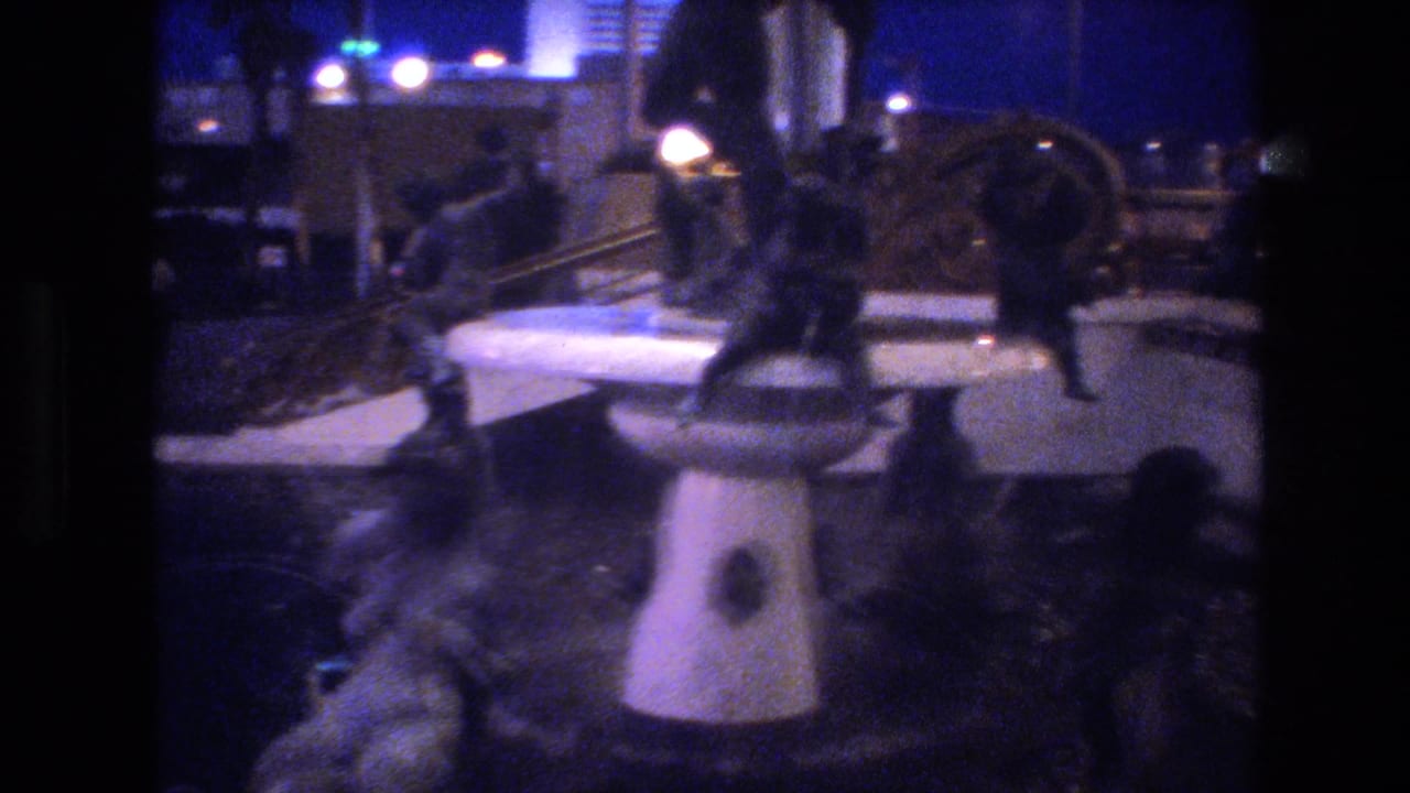 Ground-level 8mm frame of silhouetted people near a white pedestal at a nighttime outdoor event, Las Vegas area, circa 1977