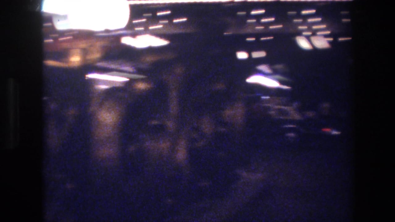 Near-black night frame with bright overhead light sources and heavy bokeh, 8mm.