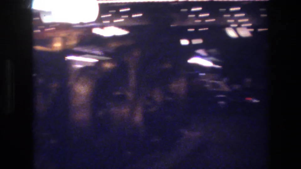 Heavily underexposed 8mm night frame showing overhead light sources with extreme bokeh defocus, consistent with 1977 Las Vegas night environment.