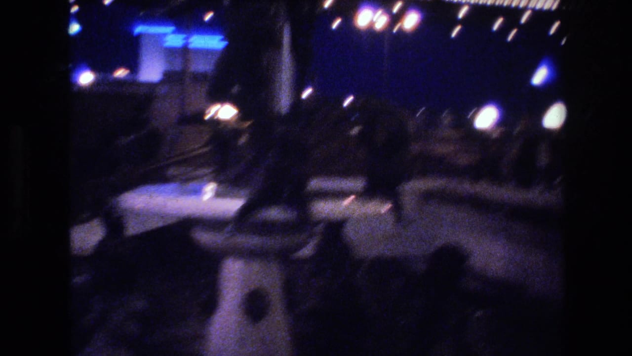 Downtown night street with walking figures and blue-illuminated signage, consistent with 1977 Las Vegas, shot on 8mm.