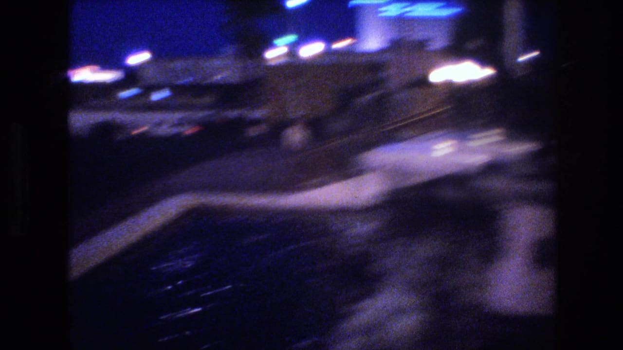 Motion-blurred night street scene shot from a moving vehicle, with streaking headlights and taillights visible.