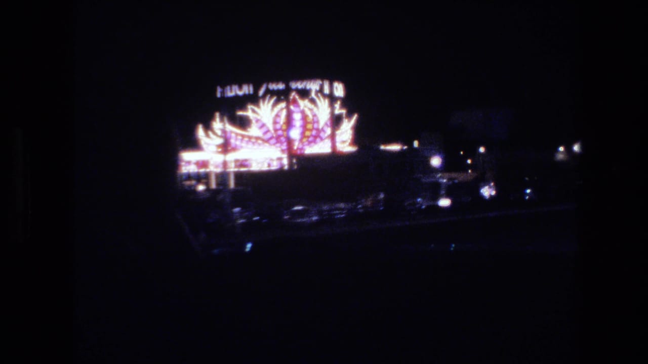 Las Vegas neon sign, 1977, captured from a car window at night; stylized feather or flame neon motifs with partially legible marquee lettering.