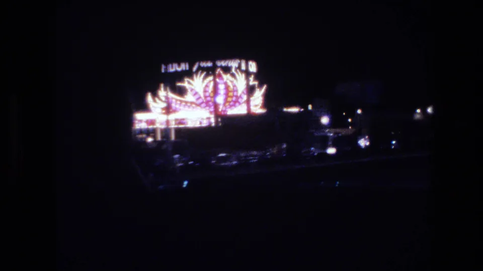 Las Vegas neon sign, 1977, captured from a car window at night; stylized feather or flame neon motifs with partially legible marquee lettering.