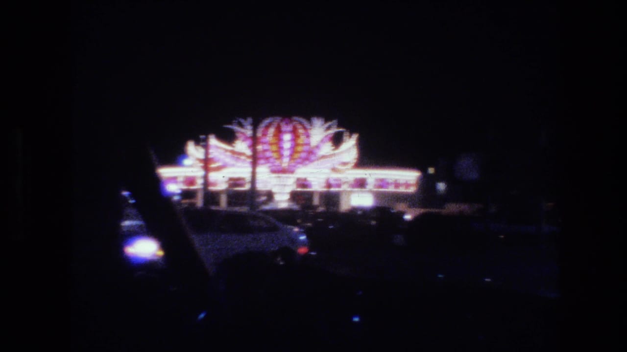 Night view from a moving car toward a brightly lit casino building and dark roadway.