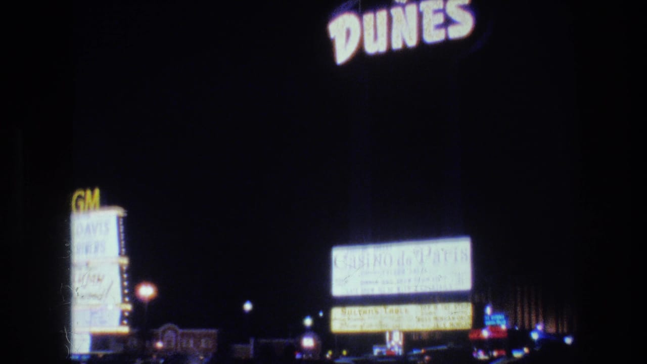 1977 Las Vegas night-drive frame with Dunes lettering in the foreground and illuminated MGM and Casino de Paris signs beyond.