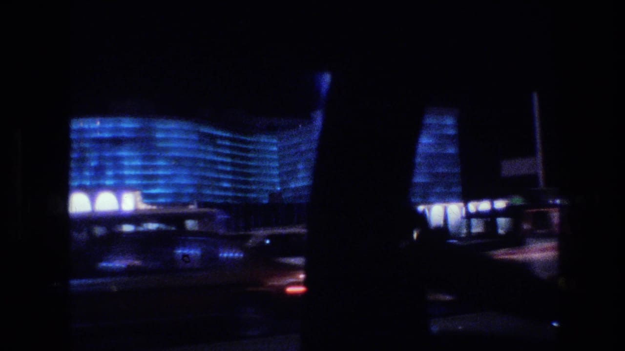 Night street view through a car window with a blue-lit curved building and dark interior pillars.