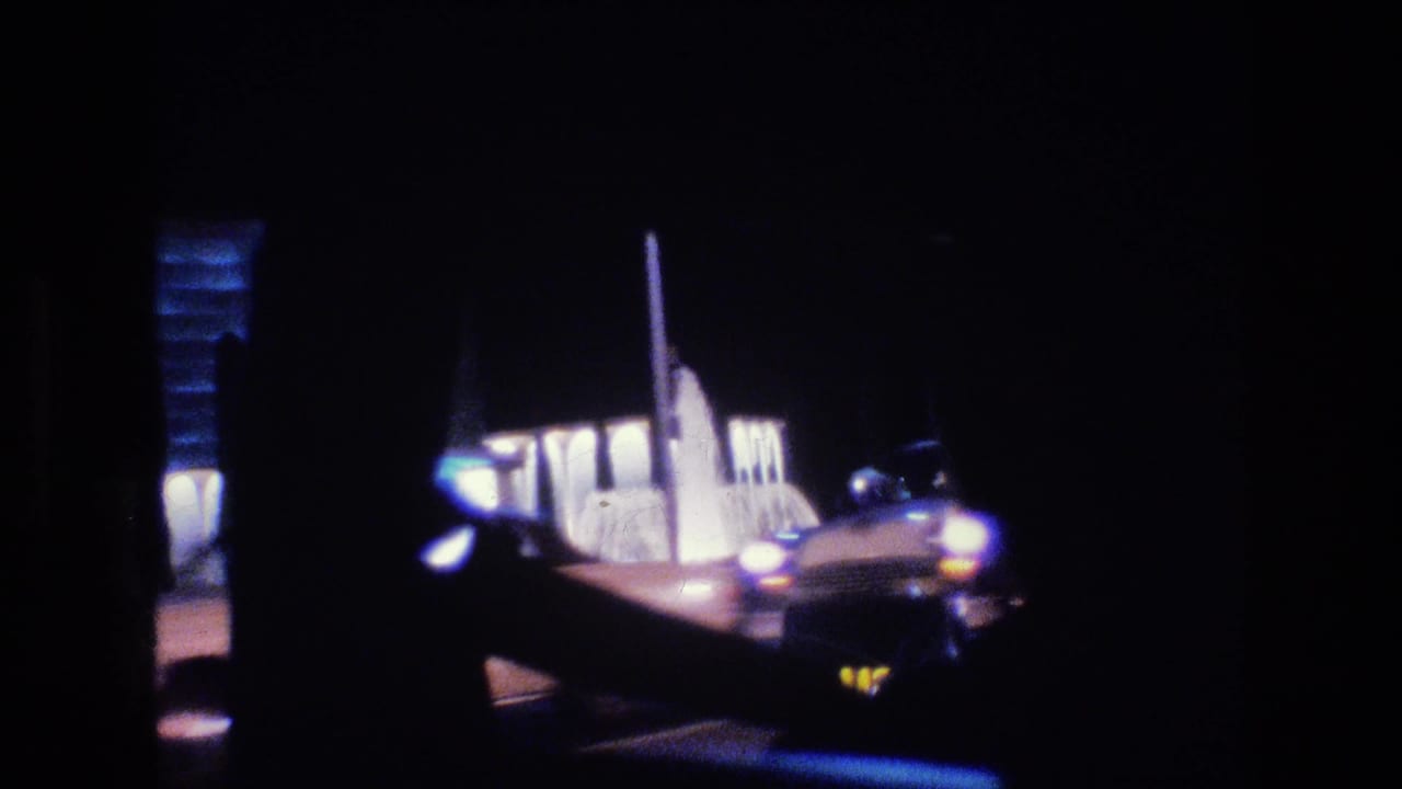 Night street scene with a car near an illuminated building seen through dark window framing.