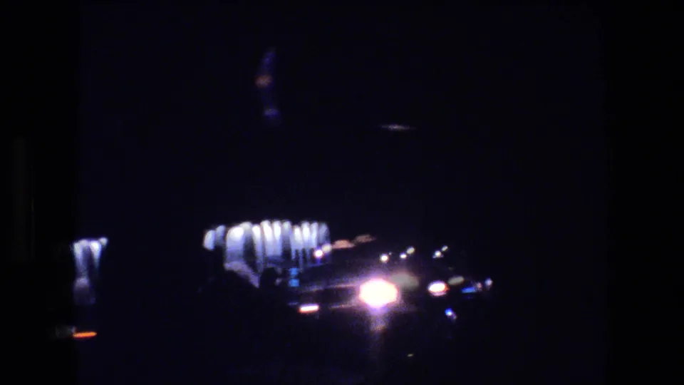 Low-light 1977 Las Vegas driving frame with bright headlamps, a roadside facade, and heavy shadow from the vehicle interior.