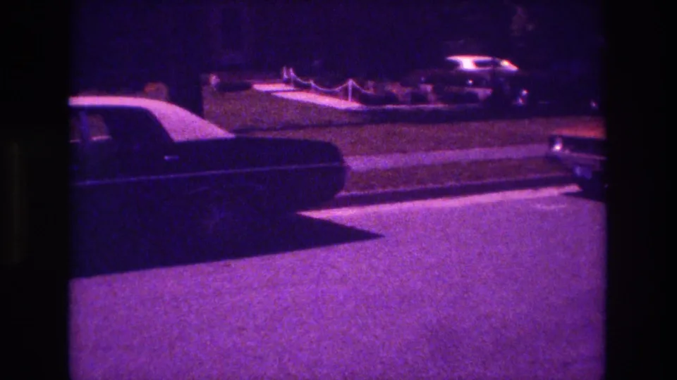 1981 San Diego 8mm frame showing a dark classic sedan entering from the left on a nighttime suburban street.