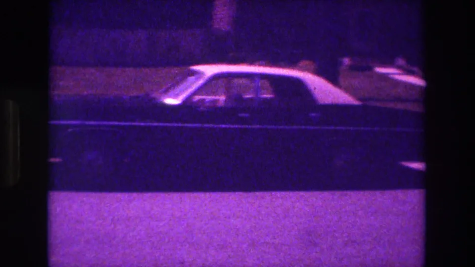 1981 San Diego 8mm frame with a dark sedan in side profile moving past a curb and grass strip at night.