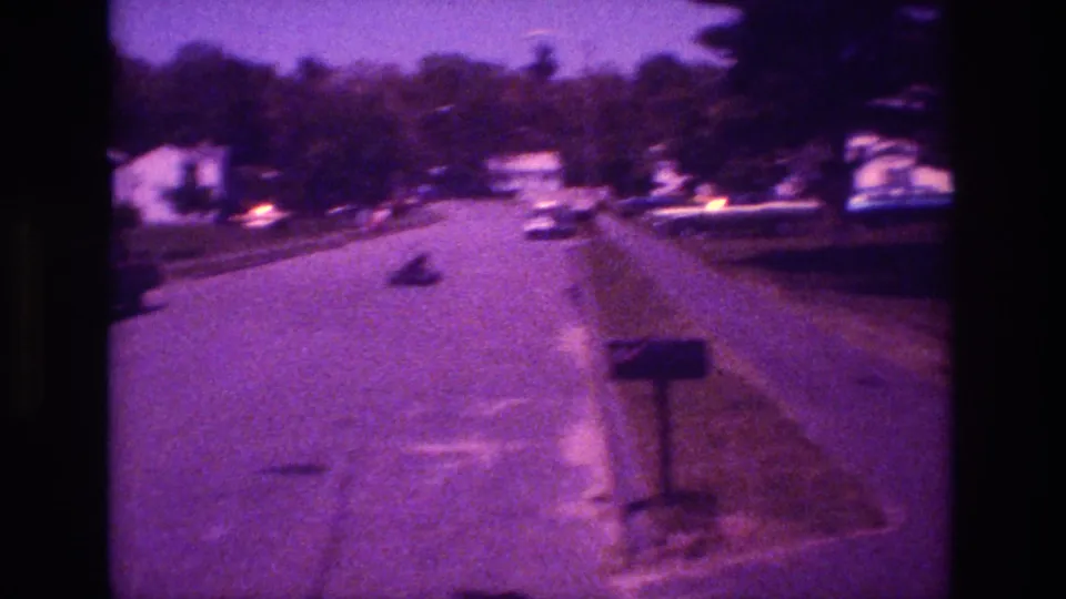 1981 San Diego home-movie frame showing a quiet residential street with parked cars, houses, trees, mailbox, and an indistinct object moving away.