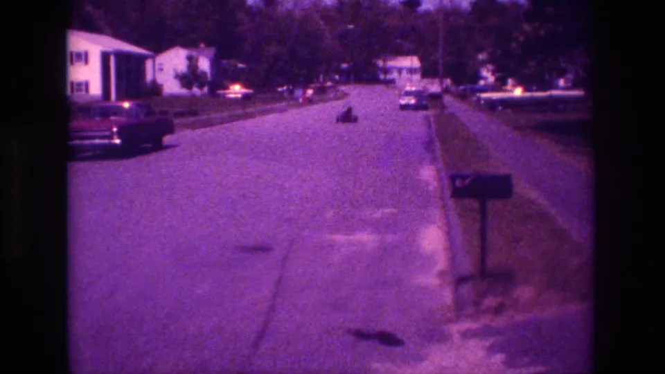 1981 San Diego frame with a soft, purple-tinted view down a suburban street as a small indistinct object recedes along the roadway.