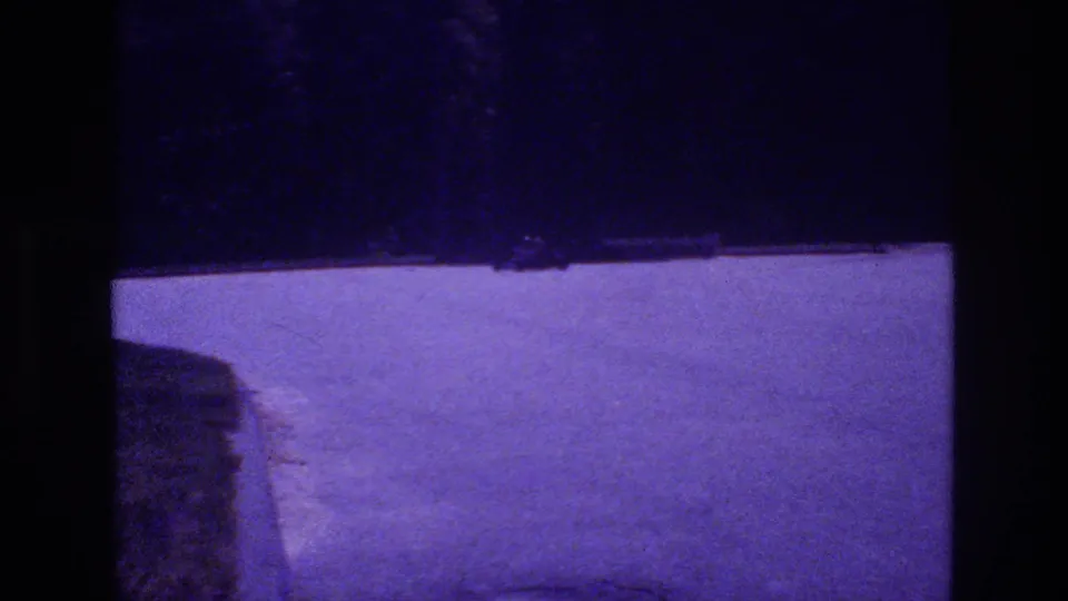 Concrete curb or raised island enters lower-left frame as the go-kart continues its arc on the purple-lit parking lot, San Diego area, 1981.