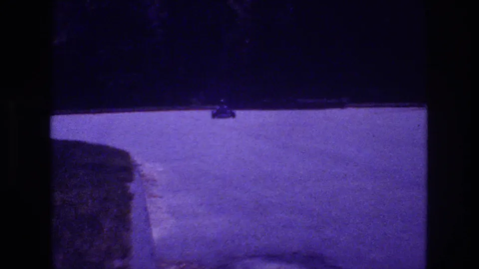 Go-kart near the end of its half-circle arc on a purple-lit parking lot with a concrete curb edge prominent in the foreground, San Diego area, 1981.