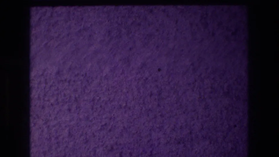Close-up of a rough popcorn stucco exterior wall in deep purple-violet light, from a 1982 8mm home movie shot in Acapulco, Mexico.
