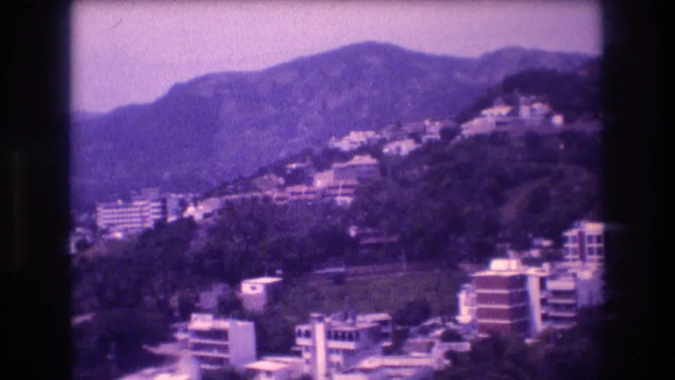 Full panoramic 8mm view of terraced residential and hotel buildings on the Acapulco hillside with mountain ridge and hazy sky, 1982.