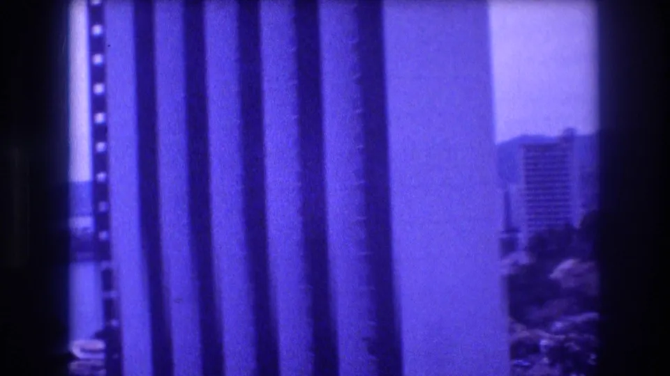 Opening frame of 1982 Acapulco 8mm home movie; film-strip borders obscure most of the image, with a high-rise and trees faintly visible.