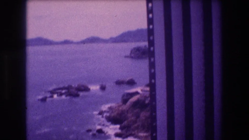 Final frame of 1982 Acapulco 8mm pan; rocky outcrops in the foreground lead across a calm bay toward rolling hills on the horizon.