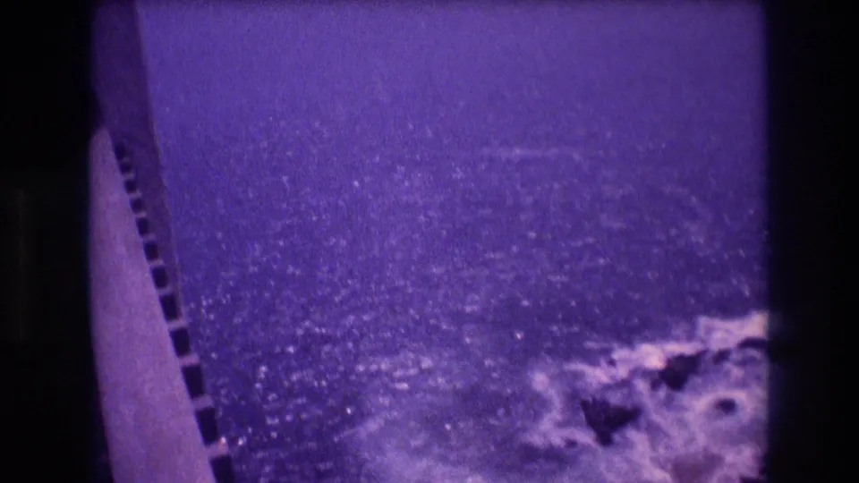 Final frame of 1982 Acapulco 8mm pan showing open Pacific Ocean surface with light glinting off water, shot from a bridge with parapet edge and film sprocket holes at border.