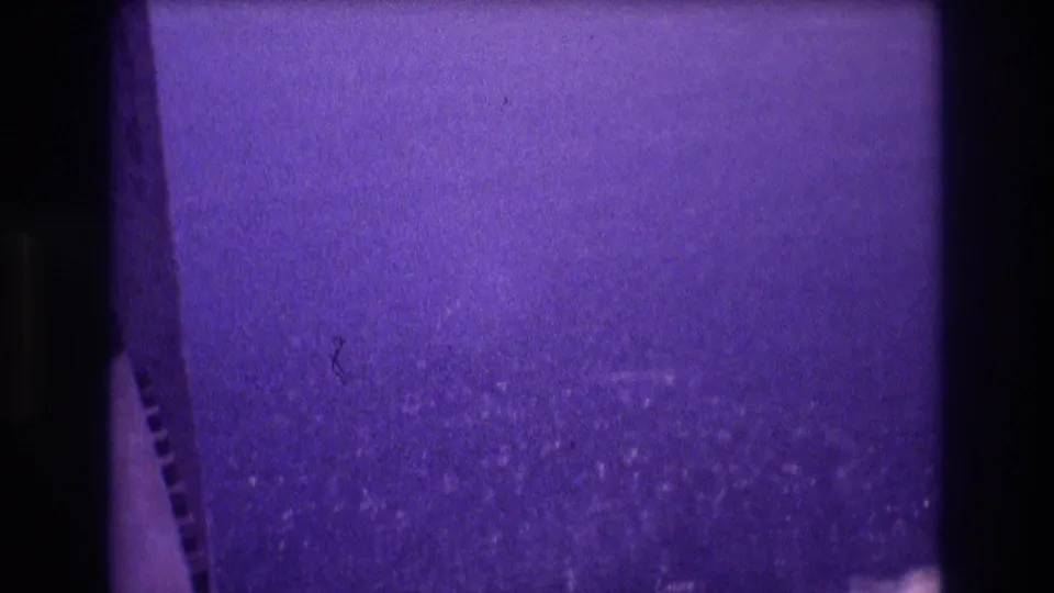 Opening frame of a 1982 Acapulco home movie with deep purple dye shift, film-perforation strip on the left edge, and a grain-heavy ocean expanse filling the lower portion.