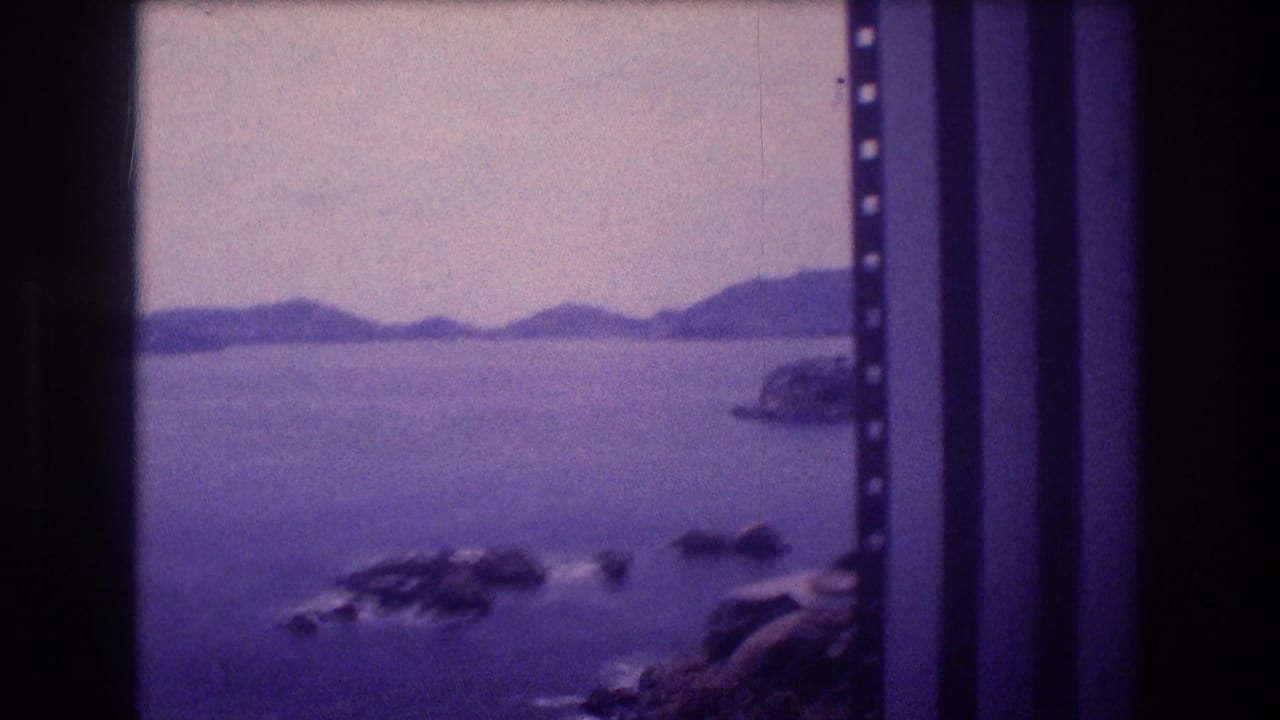 Bay view panned slightly right, showing rocky coastal outcroppings more prominently with distant hills and sprocket holes at frame edge.