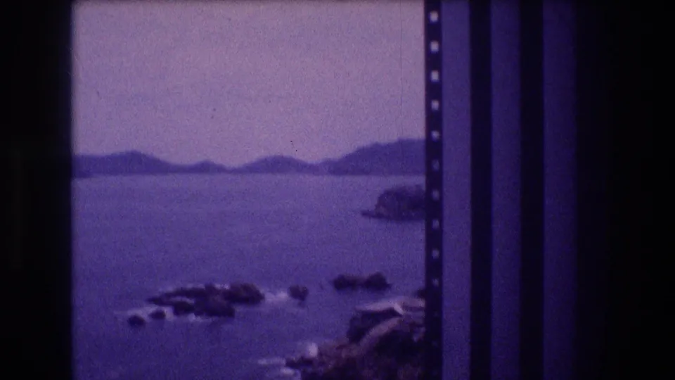 Acapulco coastline circa 1982, rocky foreground with visible wave action and distant headlands across the bay, captured on 8mm home movie film.