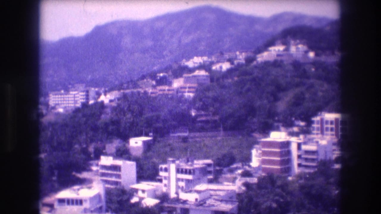 1982 8mm home-movie view from a hotel balcony showing hillside buildings, tropical vegetation, and mountain ridges, consistent with Acapulco, Mexico.