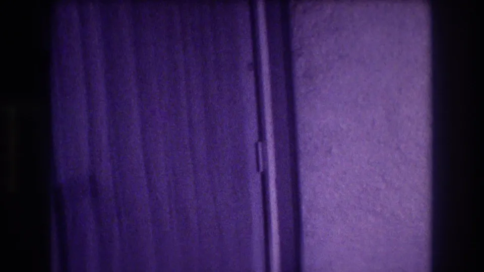 Purple-shifted 8mm home-movie frame of a sliding door and curtains in what appears to be a 1980s hotel room interior.
