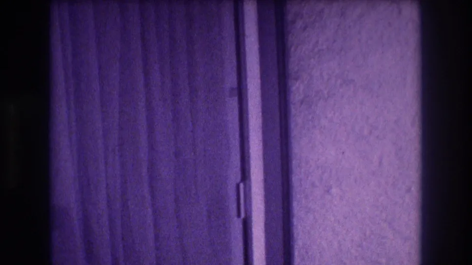 Final frame of 8mm clip showing hotel sliding door and purple curtains; color degradation consistent with aged early-1980s home-movie film.