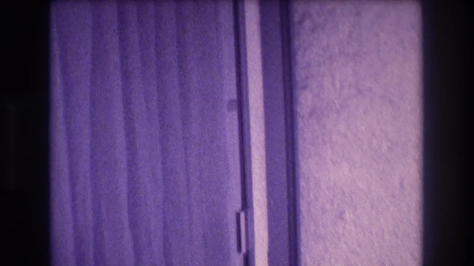 Purple-shifted 8mm home-movie frame of a draped curtain and stucco wall, consistent with an apartment interior in Acapulco, 1982