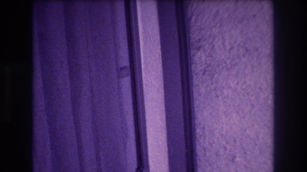 8mm home-movie frame mid-pan across draped curtain folds and a rough plaster wall with heavy purple color shift, Acapulco apartment interior, 1982