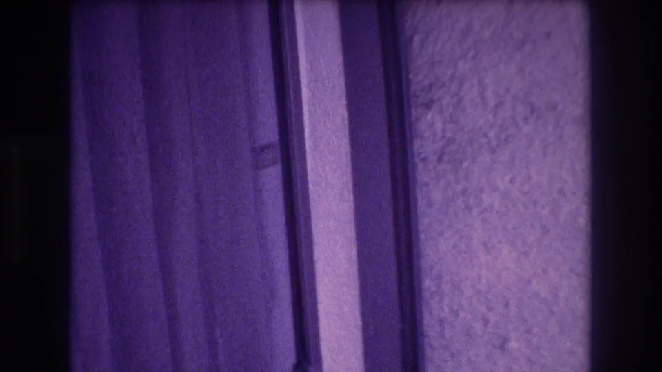 8mm home-movie frame mid-pan across draped curtain folds and a rough plaster wall with heavy purple color shift, Acapulco apartment interior, 1982