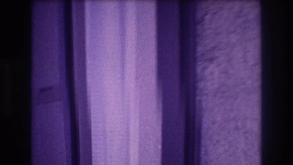 8mm home-movie frame panning past a curtain toward a door or panel edge with stucco wall visible, Acapulco apartment interior, 1982