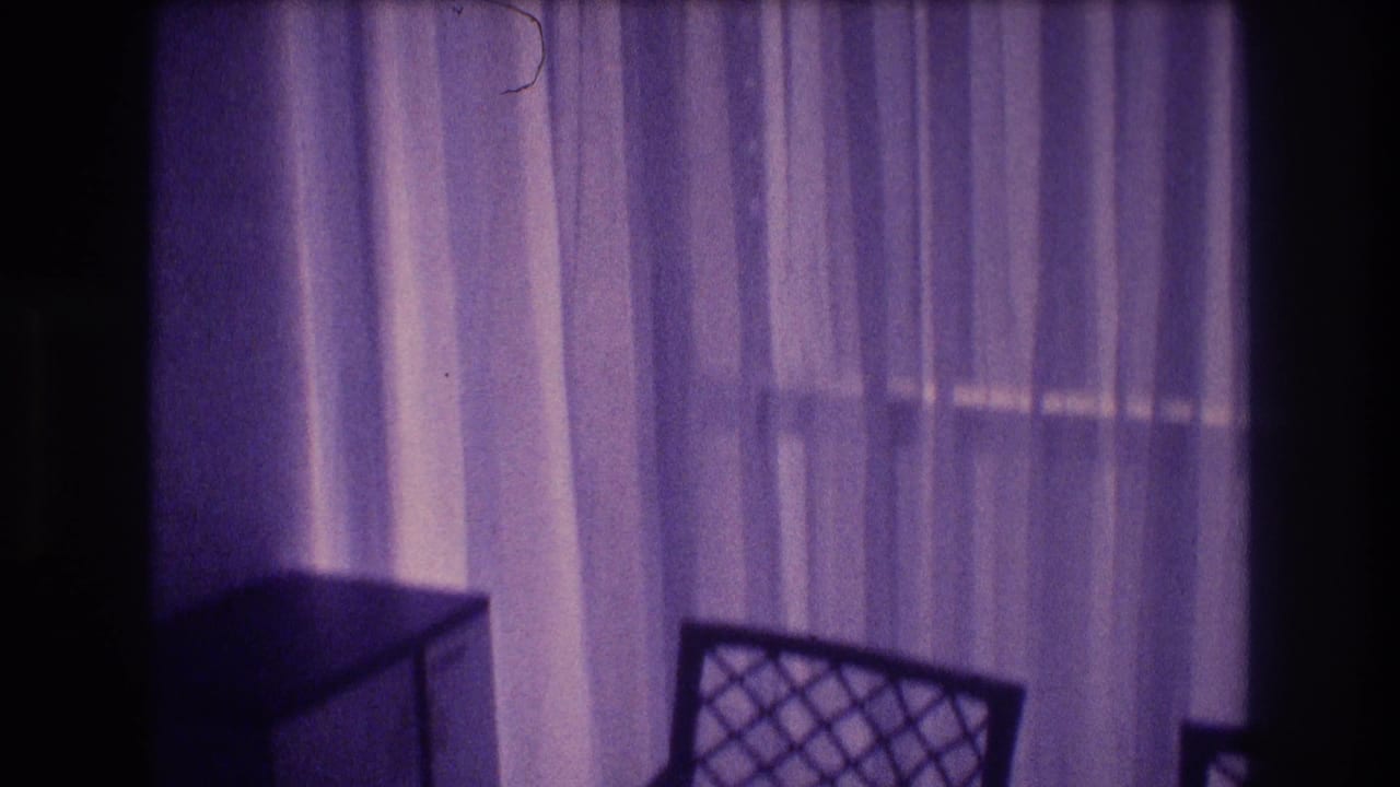 1982 8mm home movie interior: sheer curtains dominate the frame with a lattice-back chair at lower center, shot in Acapulco, Mexico with pronounced purple film color shift.
