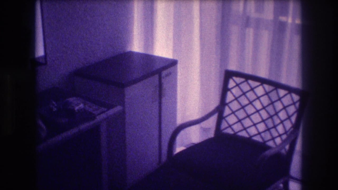 1982 8mm home movie pan revealing white nightstand and lattice-back chair in an Acapulco hotel room, purple film color shift throughout.