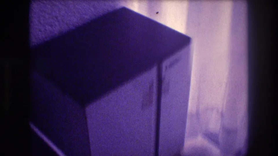 Final frame of 1982 8mm pan, white nightstand close in frame against sheer curtain backdrop in Acapulco vacation room, deep purple film color shift.