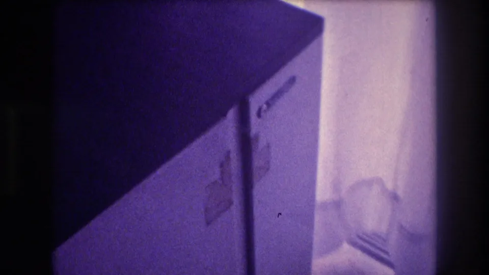 Compact white refrigerator door in mid-opening motion, dim indoor space, heavy purple Super 8 color shift, home movie footage circa 1982 Acapulco Mexico.