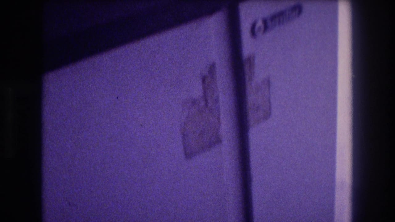 White compact refrigerator exterior showing an adhesive sticker or label, door partially in frame, heavy purple Super 8 color cast, indoor scene circa 1982.
