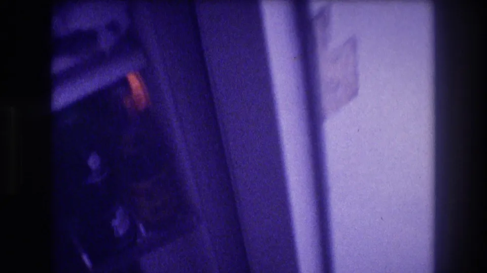 Motion-blurred 8mm pan between two refrigerators circa 1982, showing dark interior with one warm-colored label and a white wall at frame edge.