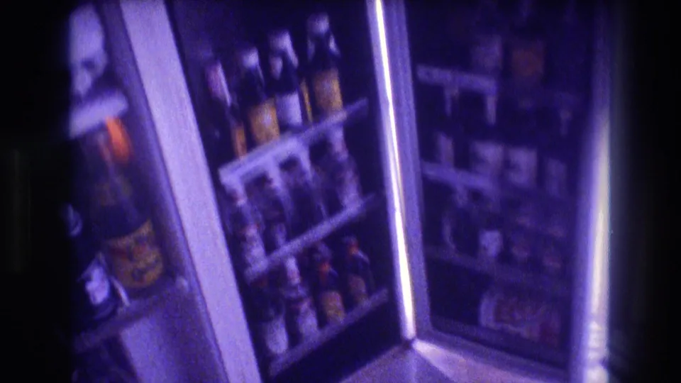 8mm home movie frame circa 1982 showing refrigerator shelves closely packed with various bottled beverages, yellow-labeled bottles prominent, heavy purple film cast.